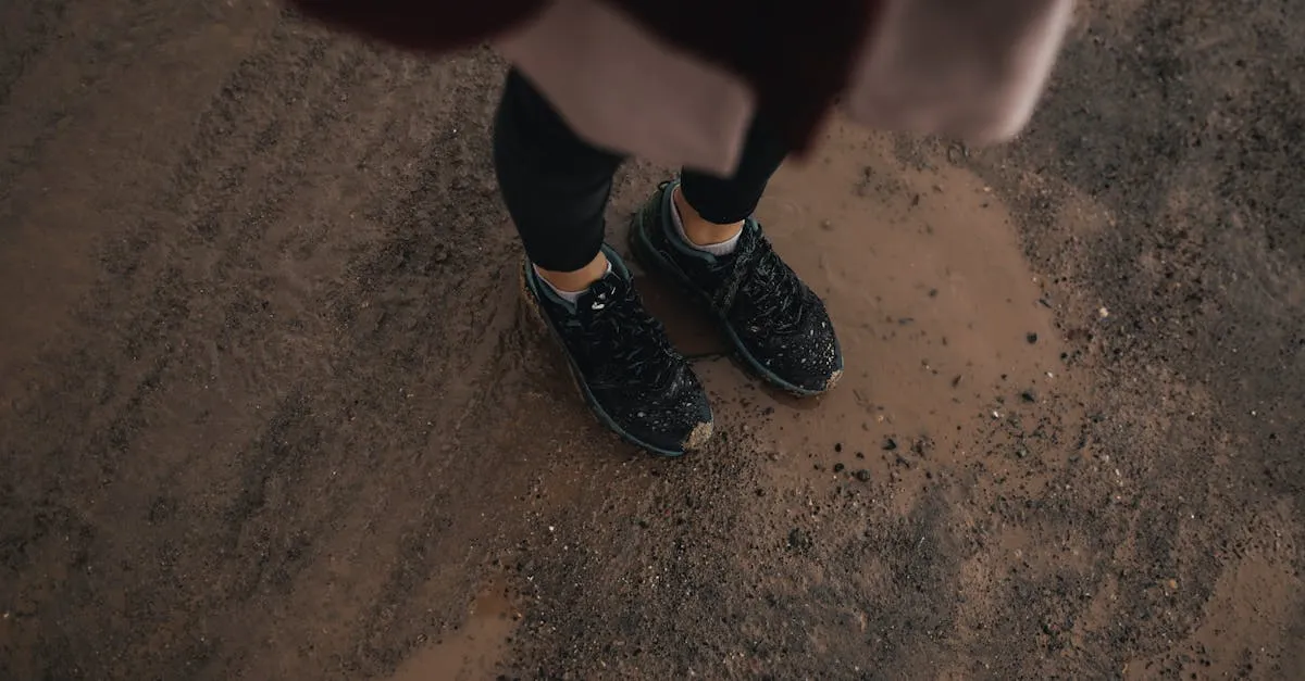 Person in sneakers standing on a muddy dirt road, captured from above.